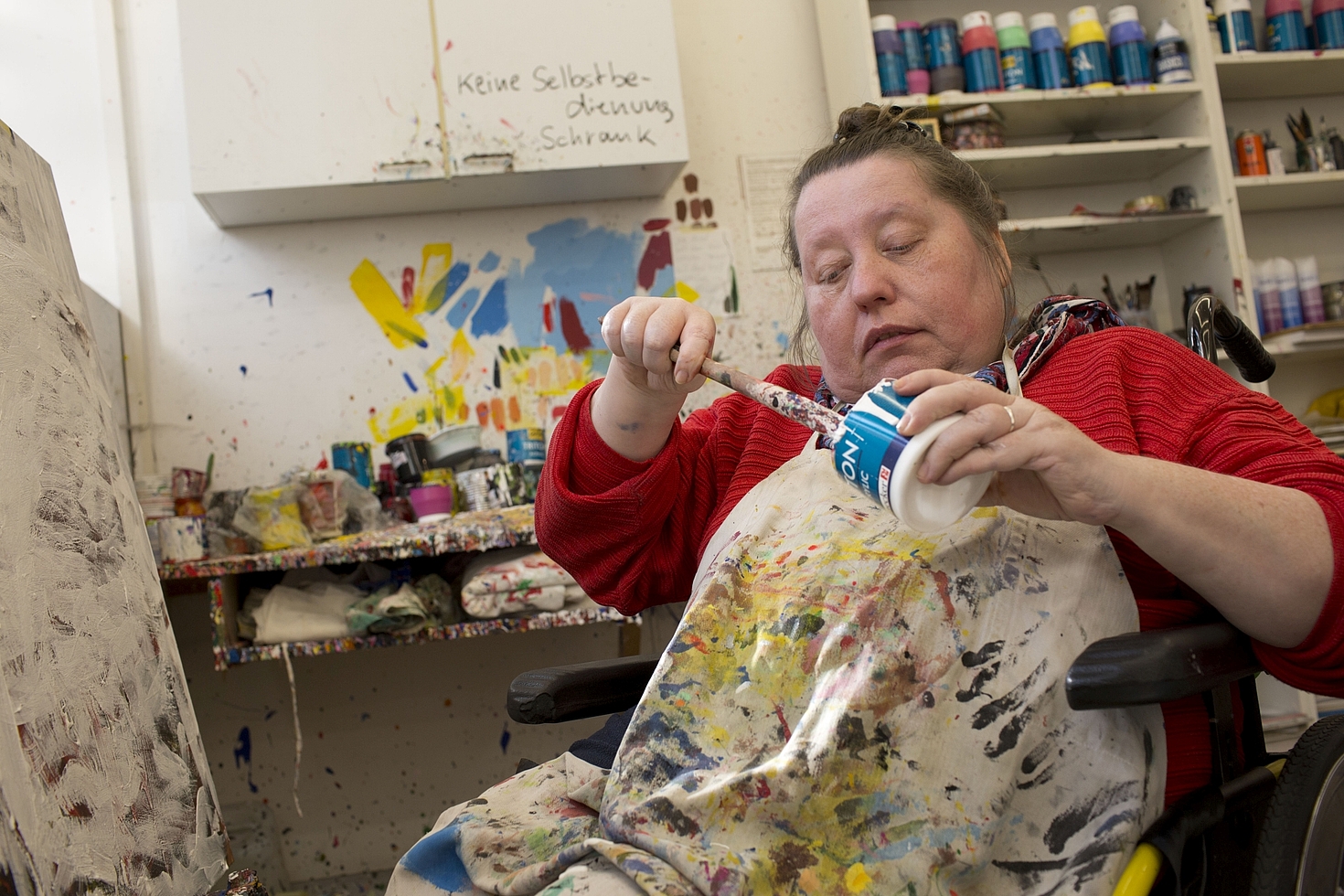 Foto: Frau im Rollstuhl malt mit bunten Farben