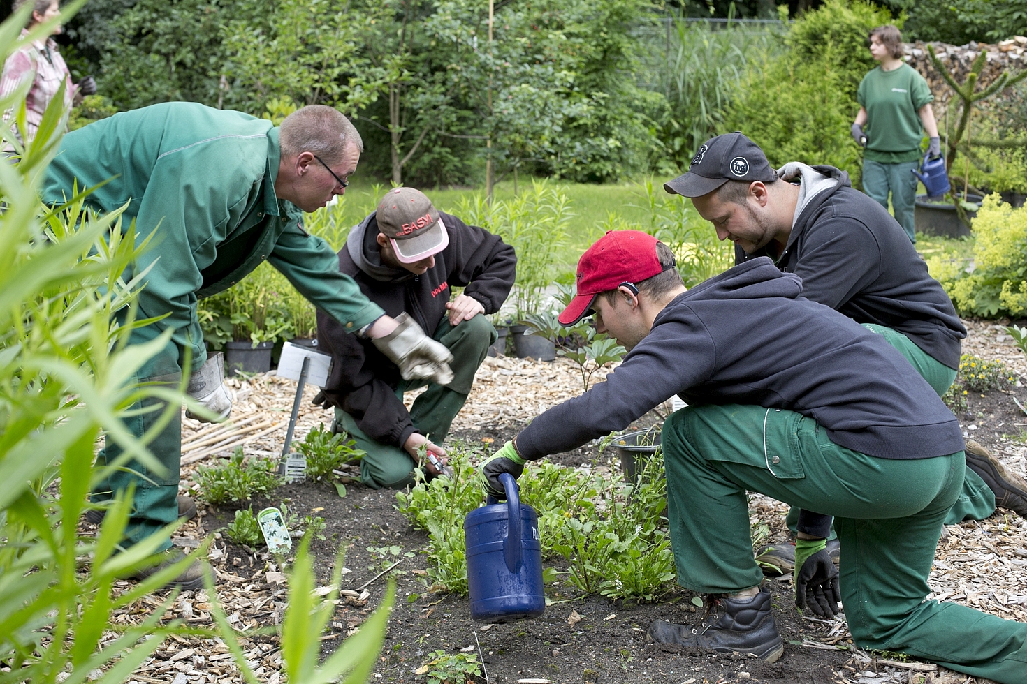 Foto: 4 Männer im Vordergrund bei der Gartenarbeit, 2 Frauen im Hintergrund