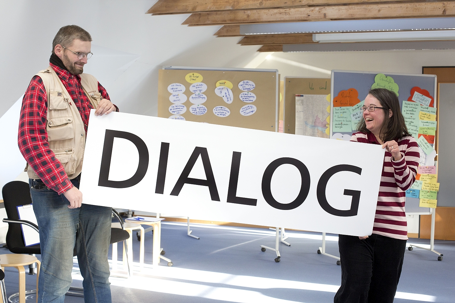 Foto: Mann und Frau halten Schild mit der Aufschrift "Dialog" zwischen sich