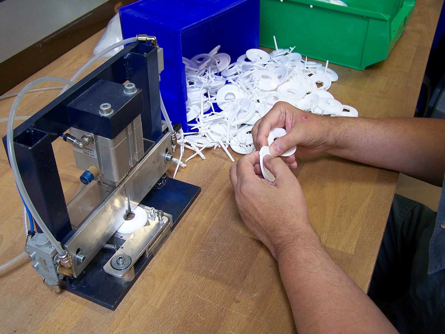 Foto: Hände arbeiten an einer Maschine mit weißen Plastikteilen