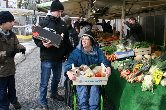 Foto: Beschäftigte mit und ohne Rollstuhl beim Einkaufen auf dem Markt
