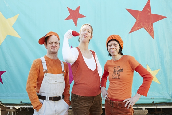 Foto: Gruppe aus einem Mann und 2 Frauen in orangenen Kostümen